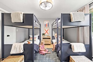 A children's room with bunk beds, a small desk, and a window with curtains.