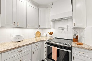 Una cocina con armarios blancos, estufa, tostadora y cafetera.