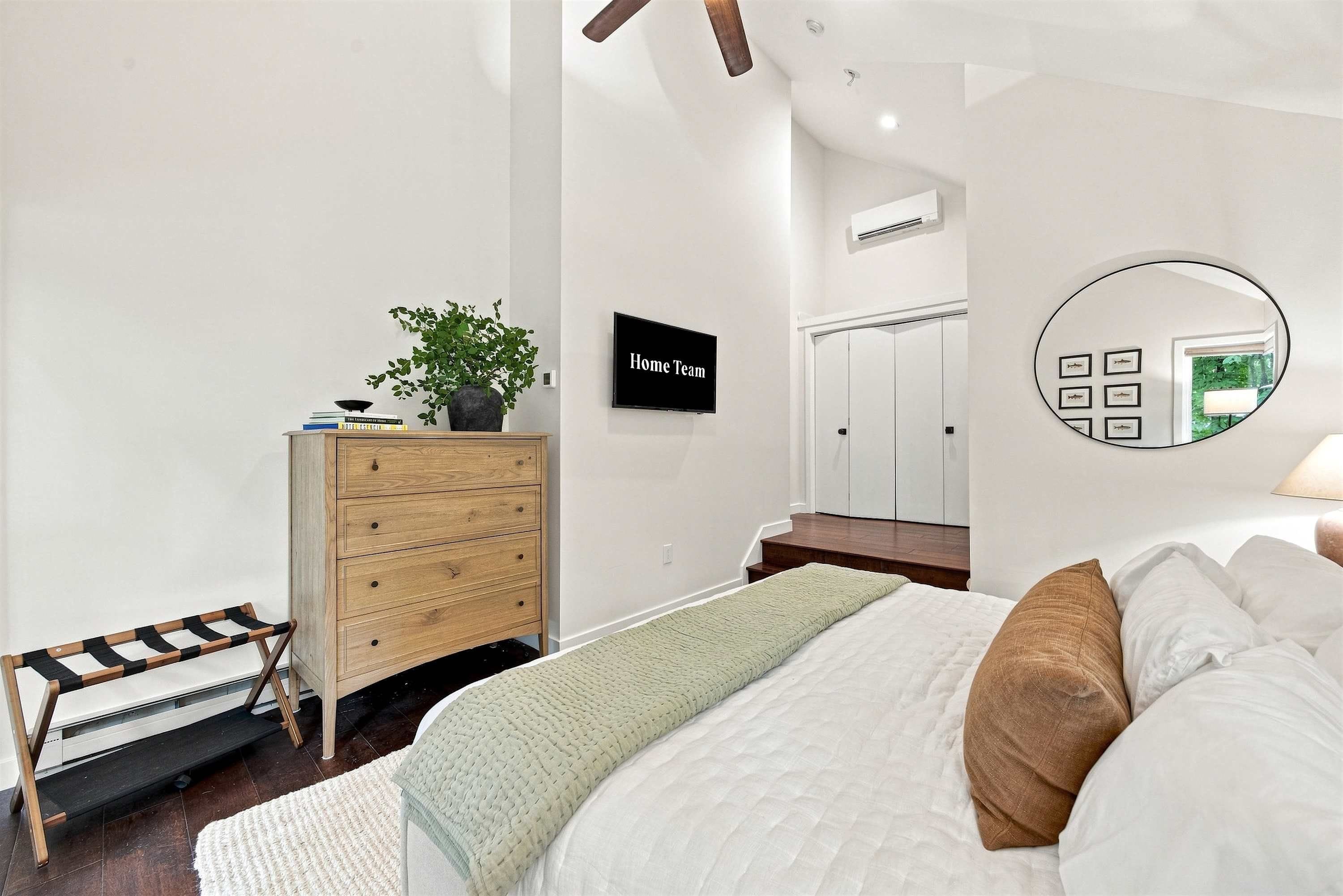 A bedroom with a bed, a dresser, a mirror, and a television.