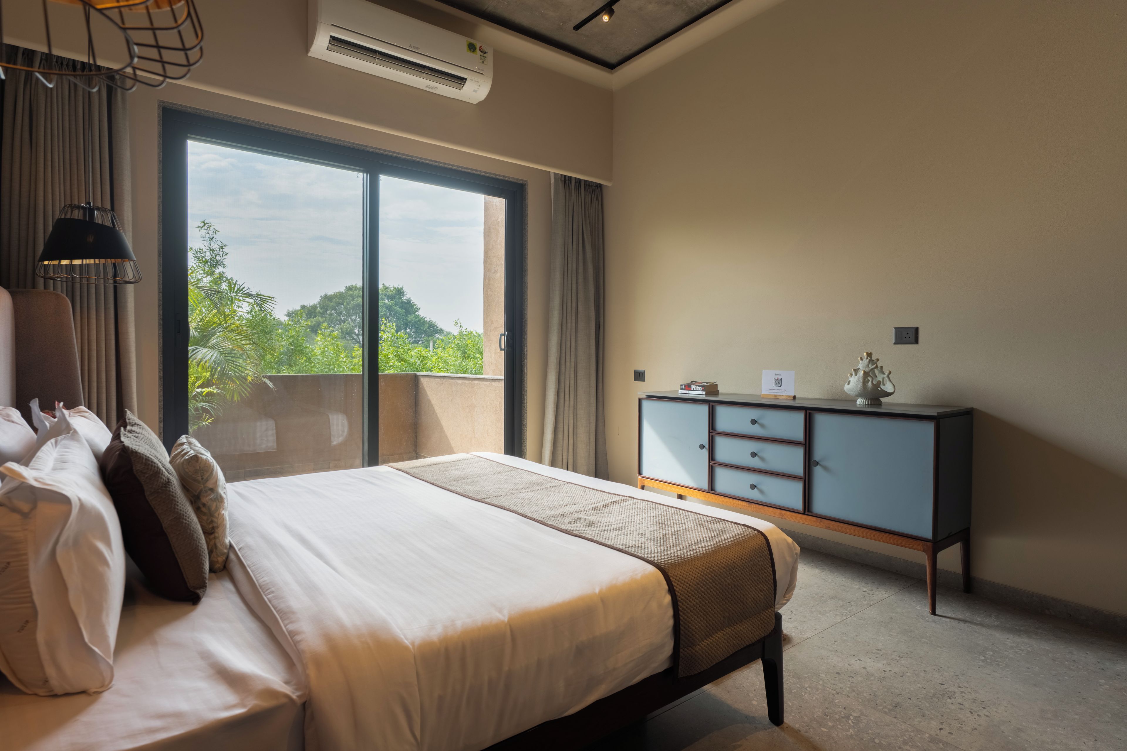 A hotel room with a large bed, a desk, and a view of greenery outside.