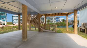 Ein überdachter Außenbereich mit einer Holztreppe, die zu einer Terrasse führt, umgeben von Gebäuden und einem Gewässer.