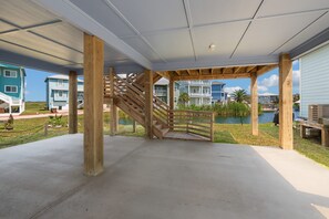 Ein überdachter Außenbereich mit einer Holztreppe, die zu einer Terrasse führt, umgeben von Gebäuden und einem Gewässer.
