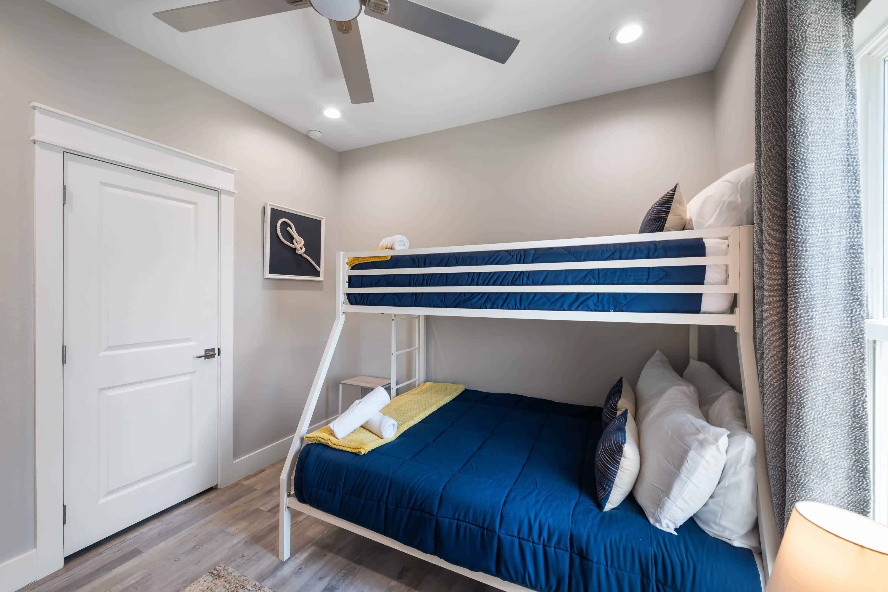 A bunk bed with a blue mattress and white headboard, a ceiling fan, a white door, and a small framed picture on the wall.