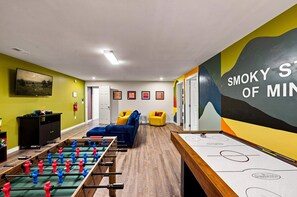 A room with a foosball table, a sofa, and a wall with a painting. - Rolling Hills Retreat Hot Tub Fire Pit Sauna (Sevierville)