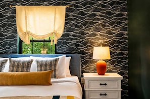 Ein Schlafzimmer mit einem Bett, Kissen, einem Nachttisch, einer Lampe und einem Fenster mit Blick.