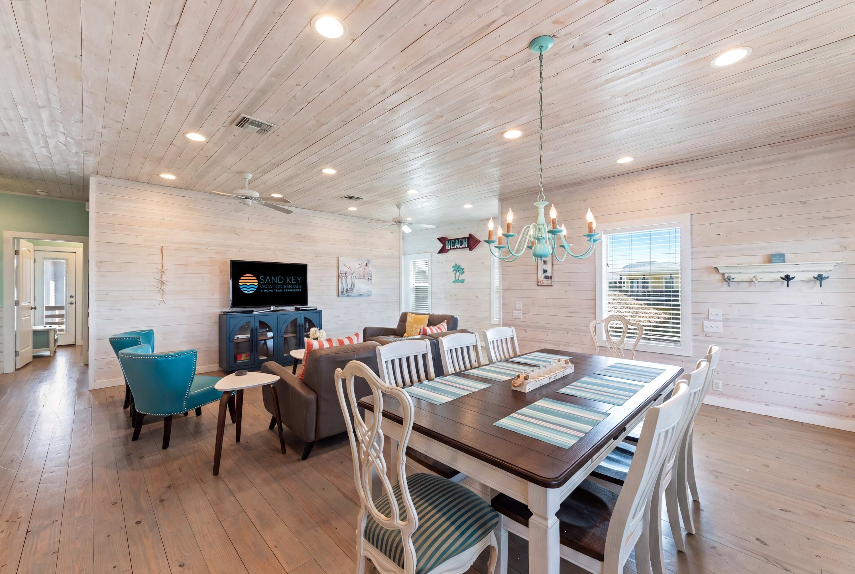 A spacious room with a wooden ceiling, a dining table with chairs, a television, and a chandelier.
