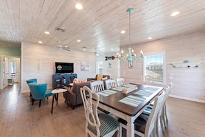 A spacious room with a wooden ceiling, a dining table with chairs, a television, and a chandelier. - Port A Vallarta Community Pool Close to Beach (Port Aransas)