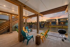 Une terrasse extérieure avec des poutres en bois, des fauteuils Adirondack aux couleurs vives, un hamac et un barbecue.