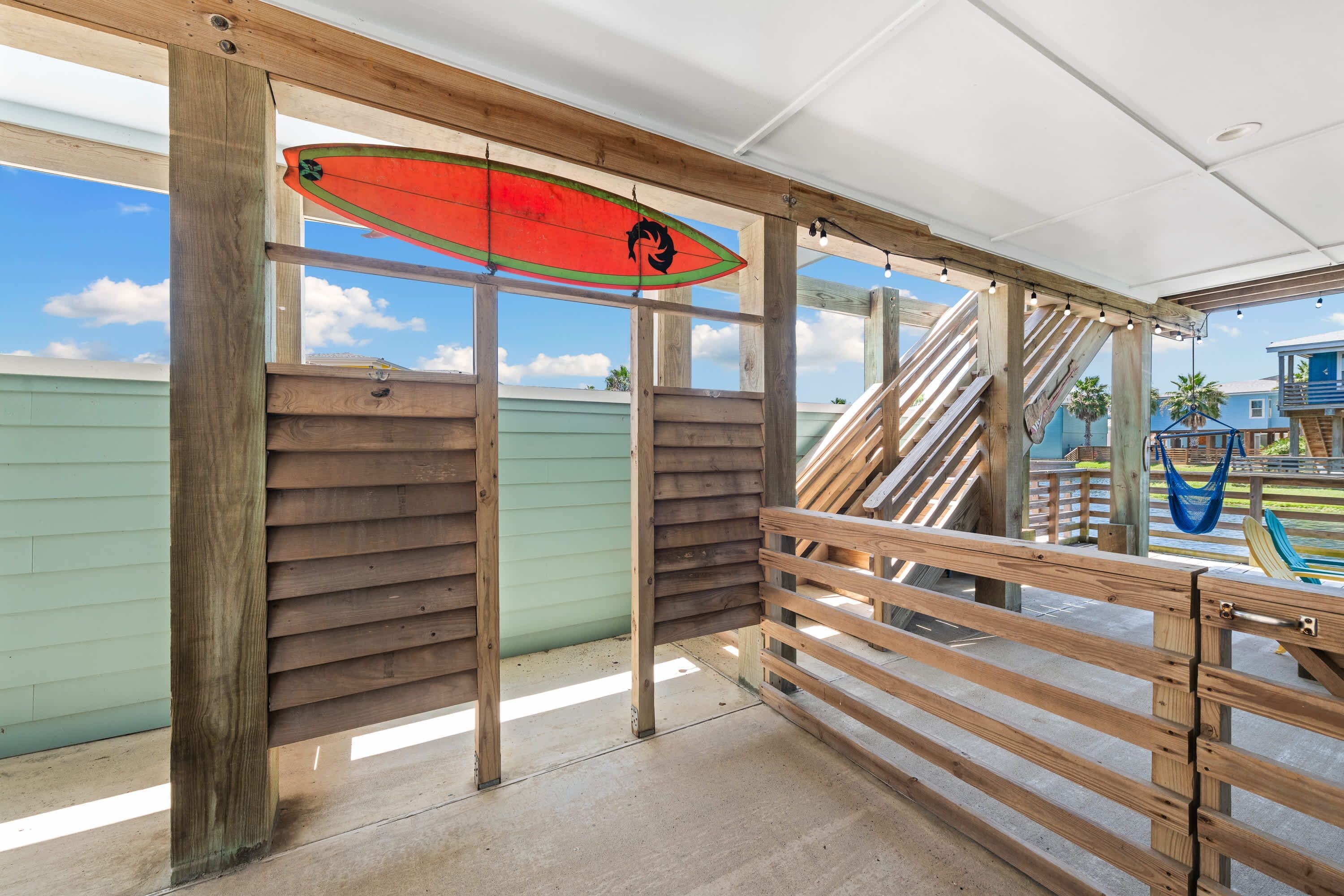 A wooden deck with a surfboard, a staircase, and a view of a building.