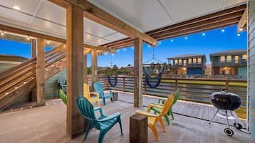 An outdoor patio with wooden beams, colorful Adirondack chairs, a hammock, and a barbecue grill.