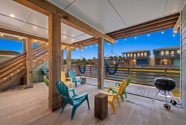 An outdoor patio with wooden beams, colorful Adirondack chairs, a hammock, and a barbecue grill. - Port A Vallarta Community Pool Close to Beach (Port Aransas)