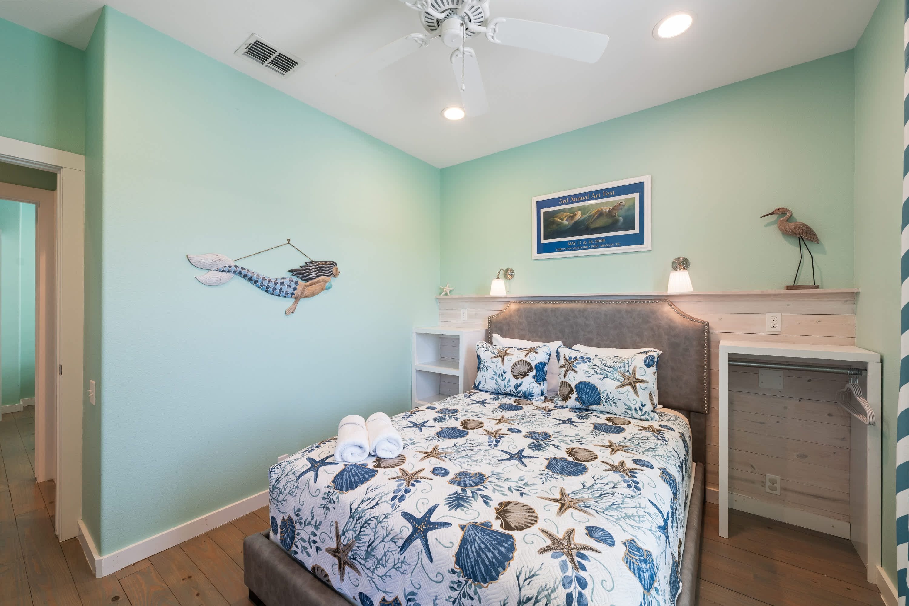 Une chambre à coucher comprenant un lit, un ventilateur de plafond, une œuvre d’art accrochée au mur et un élément décoratif mural.