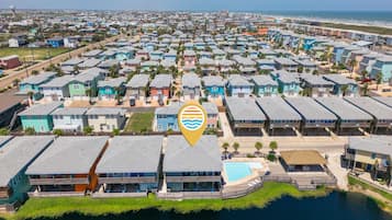 An aerial view of a coastal residential area with multiple two-story houses, a swimming pool, and a beachfront.
