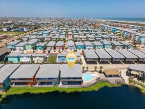 An aerial view of a coastal residential area with multiple two-story houses, a swimming pool, and a beachfront. - Port A Vallarta Community Pool Close to Beach (Port Aransas)