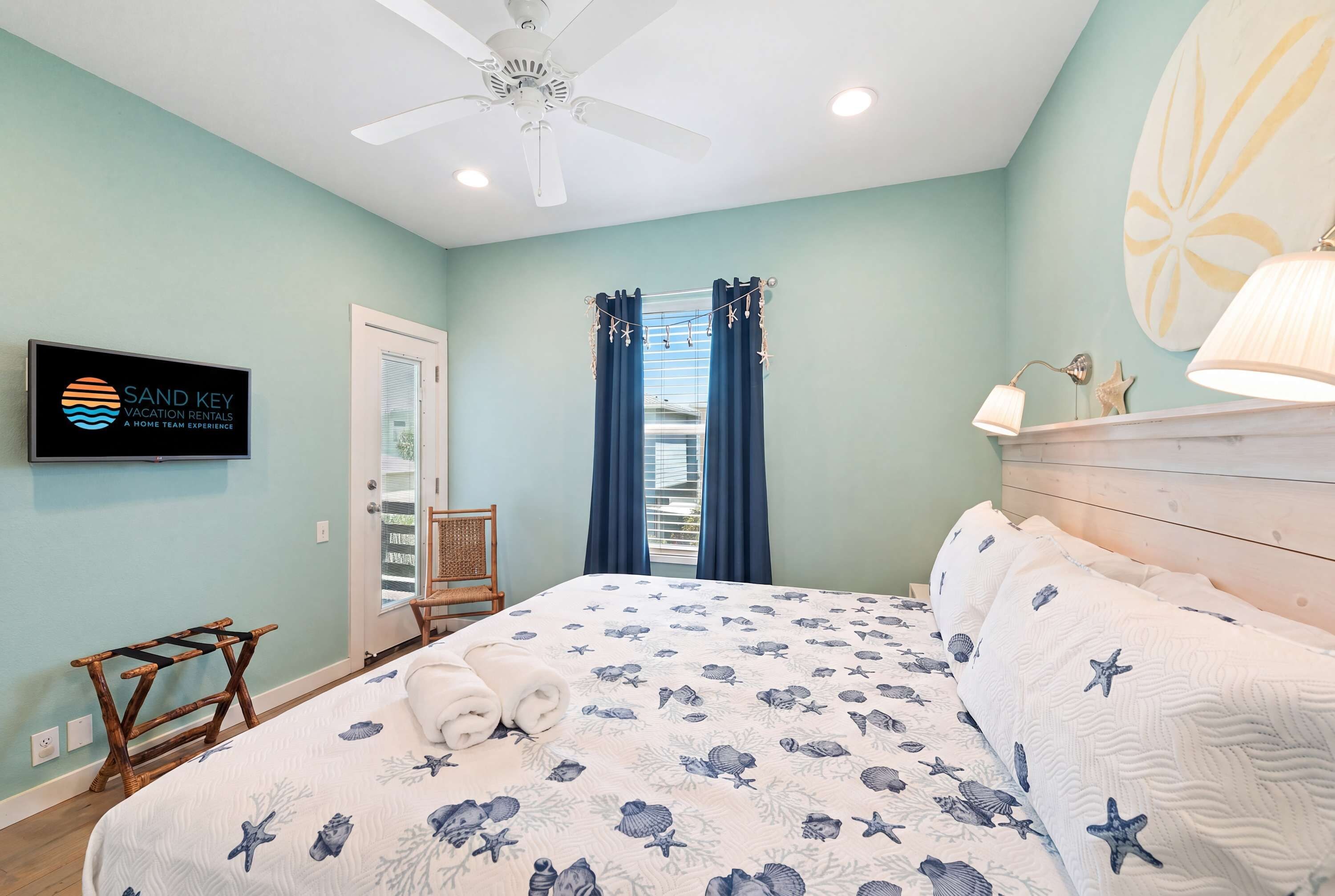 A bedroom with a bed, a ceiling fan, a TV, and a window with curtains.