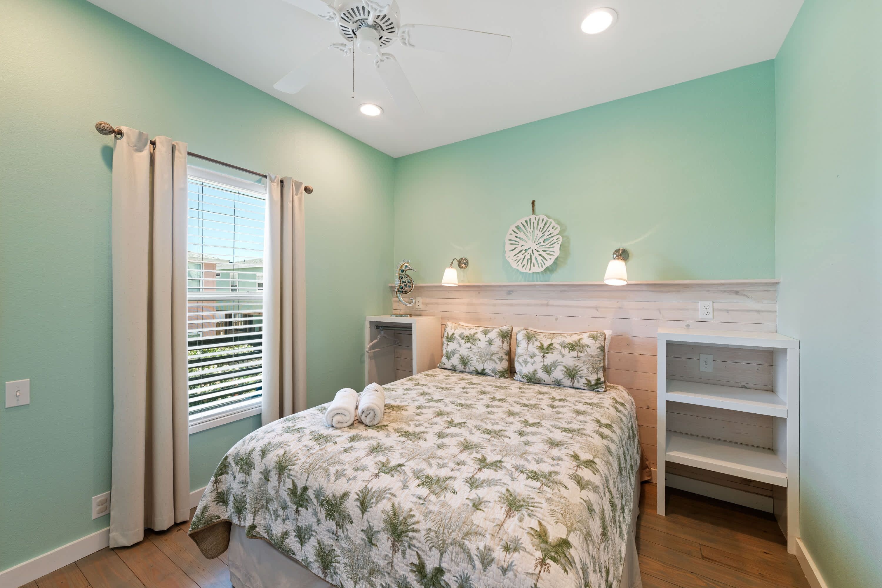 A bedroom with a bed, a window with curtains, a ceiling fan, and a wall-mounted light fixture.