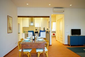 A dining area with a table set for four, a kitchen in the background, a television on a cabinet, and an air conditioning unit on the wall. - Sunny & Spacious Apartment in the Heart of Lucca (Lucca)