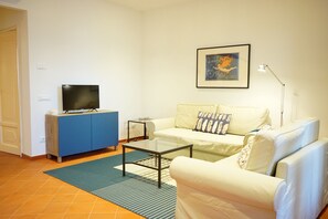A living room with a sofa, a coffee table, a TV on a blue cabinet, a framed picture on the wall, and a lamp. - Sunny & Spacious Apartment in the Heart of Lucca (Lucca)