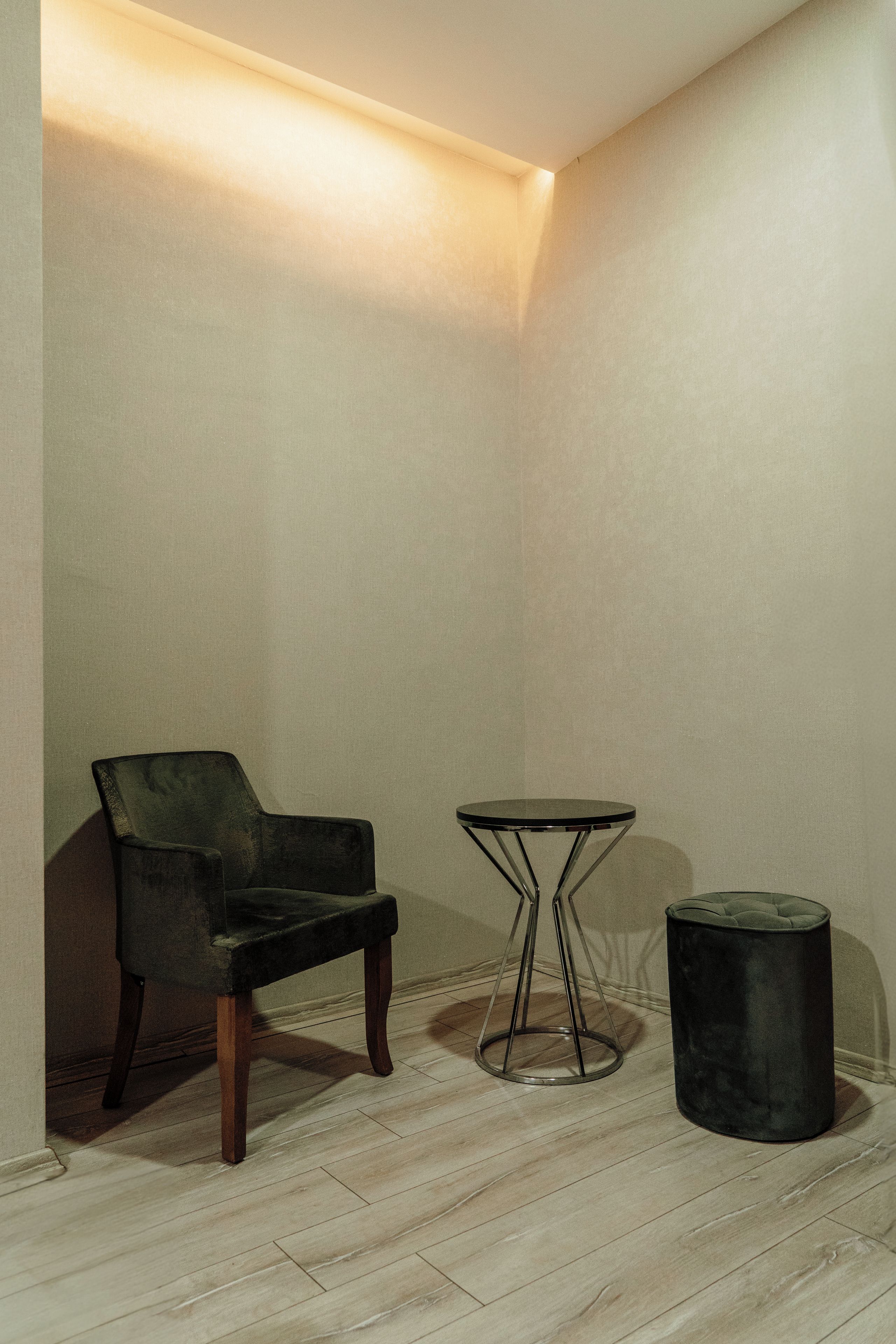 A corner room with a chair, a small round table, and a round ottoman.