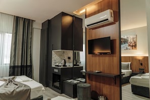 A modern hotel room with a flat-screen TV, a minibar, a wooden panel wall, and a bed with a headboard. - TİTİZ HOTEL (Gaziantep)