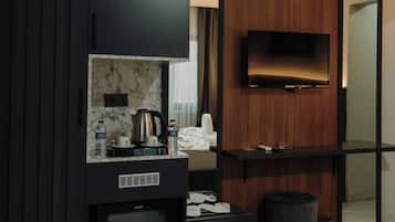Una camera d'albergo moderna con televisione a schermo piatto, angolo cottura completo di macchina del caffè e cestino.