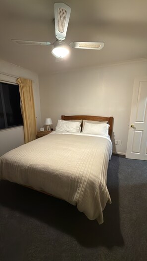 Quarto de hotel com cama, mesa de cabeceira, abajur, janela com cortinas e porta.