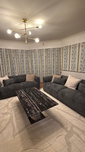 Sala de estar com um sofá seccional cinza escuro, uma mesa de centro de mármore preto e um lustre.