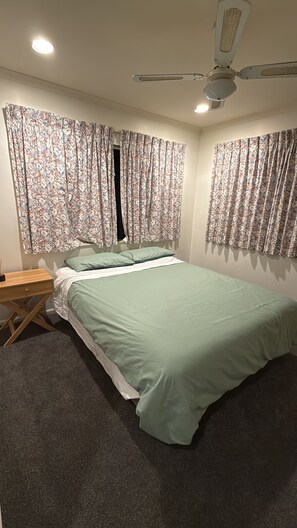 Ein Schlafzimmer mit Bett, Vorhängen, einem Nachttisch, einem Schreibtisch und einem Deckenventilator.