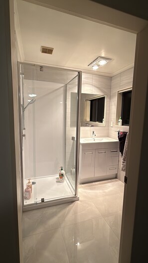 Ein modernes Badezimmer mit einer gläsernen Duschkabine, einem Waschtisch mit Spiegel und einer Toilette.