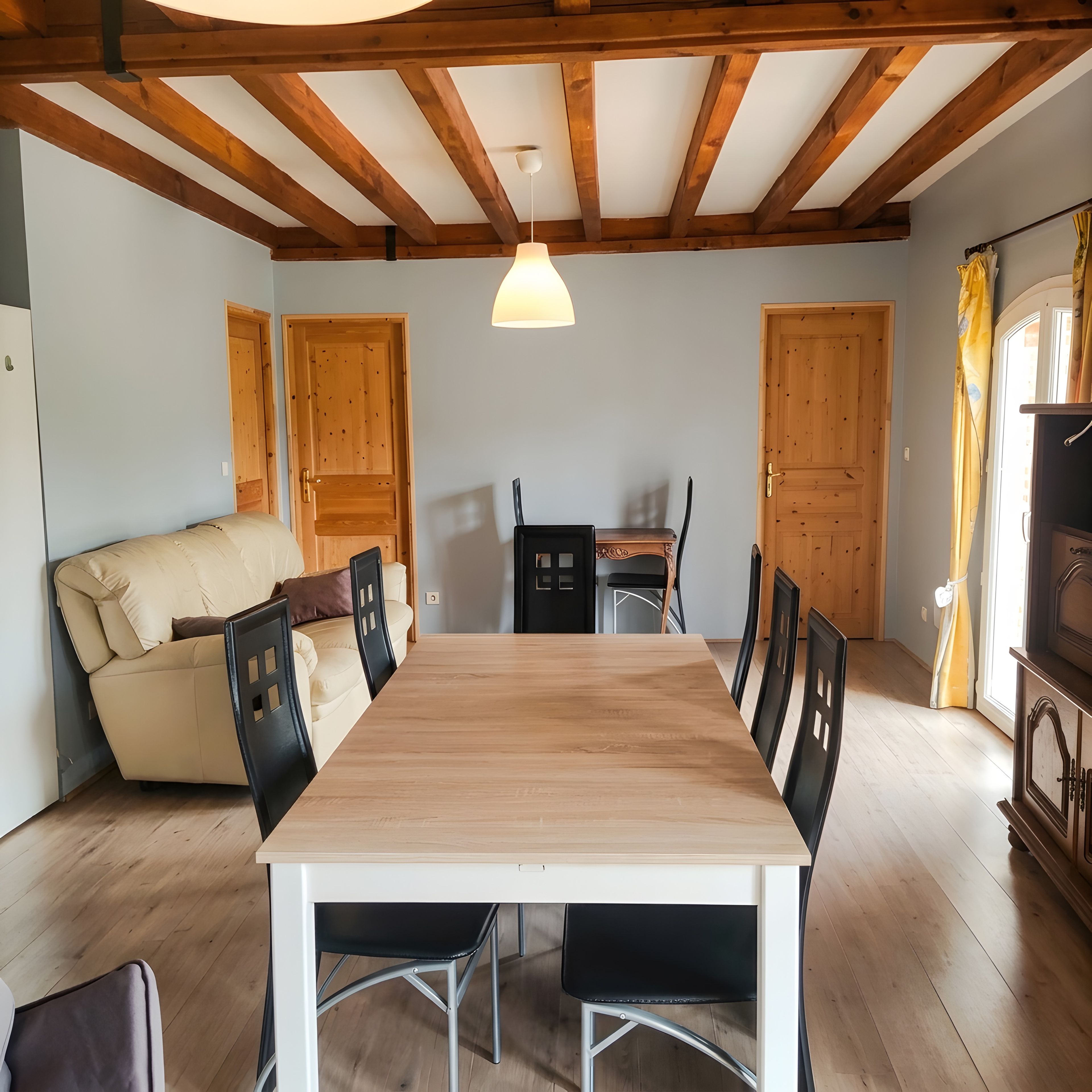 Un comedor con mesa y sillas de madera, un sofá y puertas de madera.