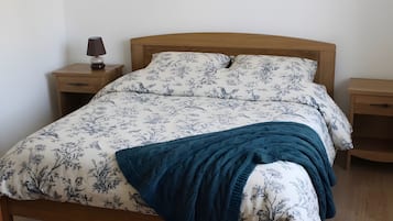 A bed with a floral pattern bedspread, a dark blue throw blanket, and wooden nightstands with a lamp.