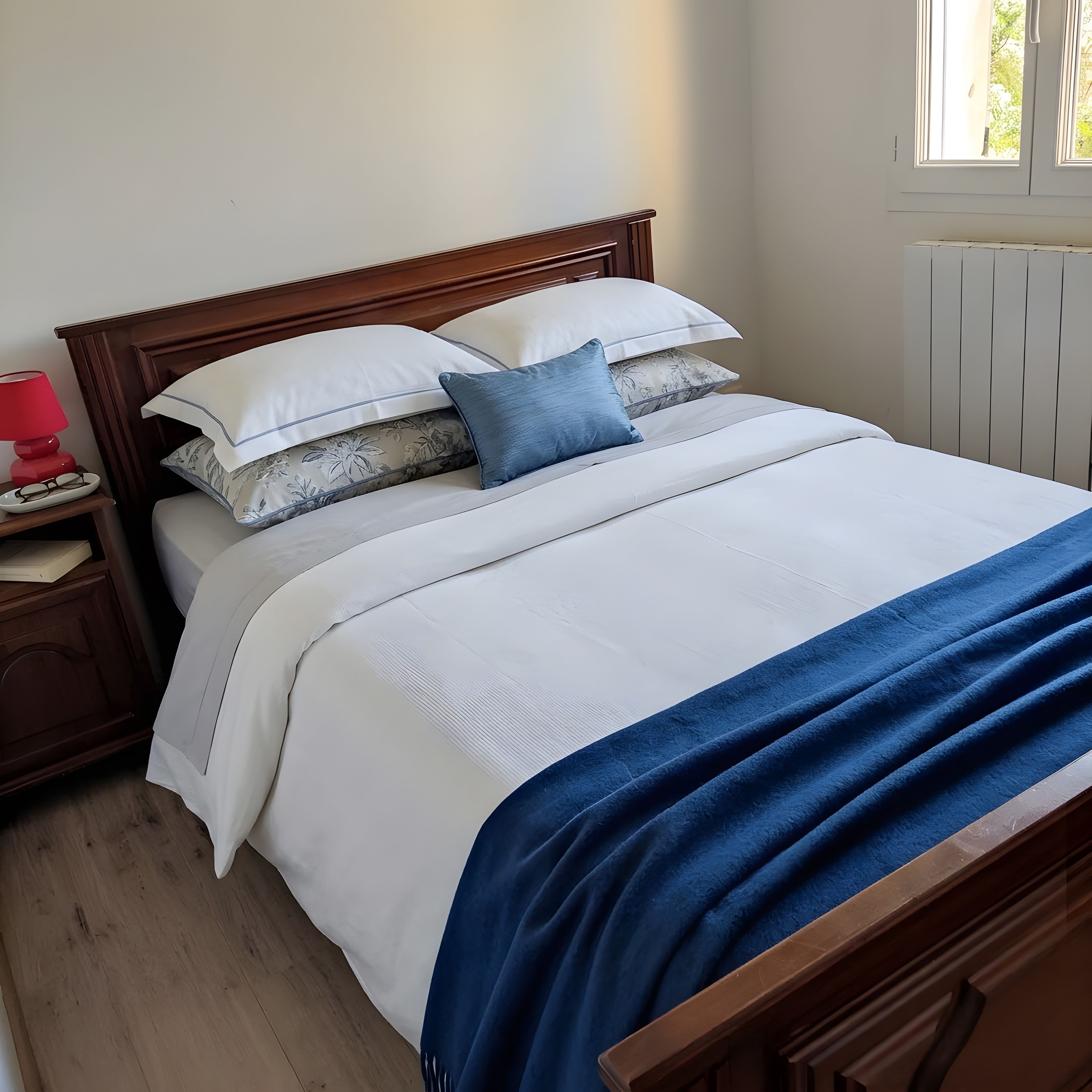 A neatly made bed with a white and blue bedding set, a wooden headboard, and a bedside table with a lamp.