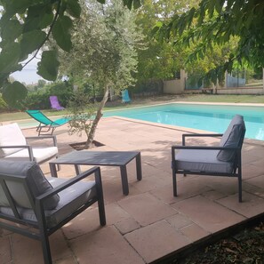 Un espace extérieur avec une piscine, des chaises longues et un petit arbre.