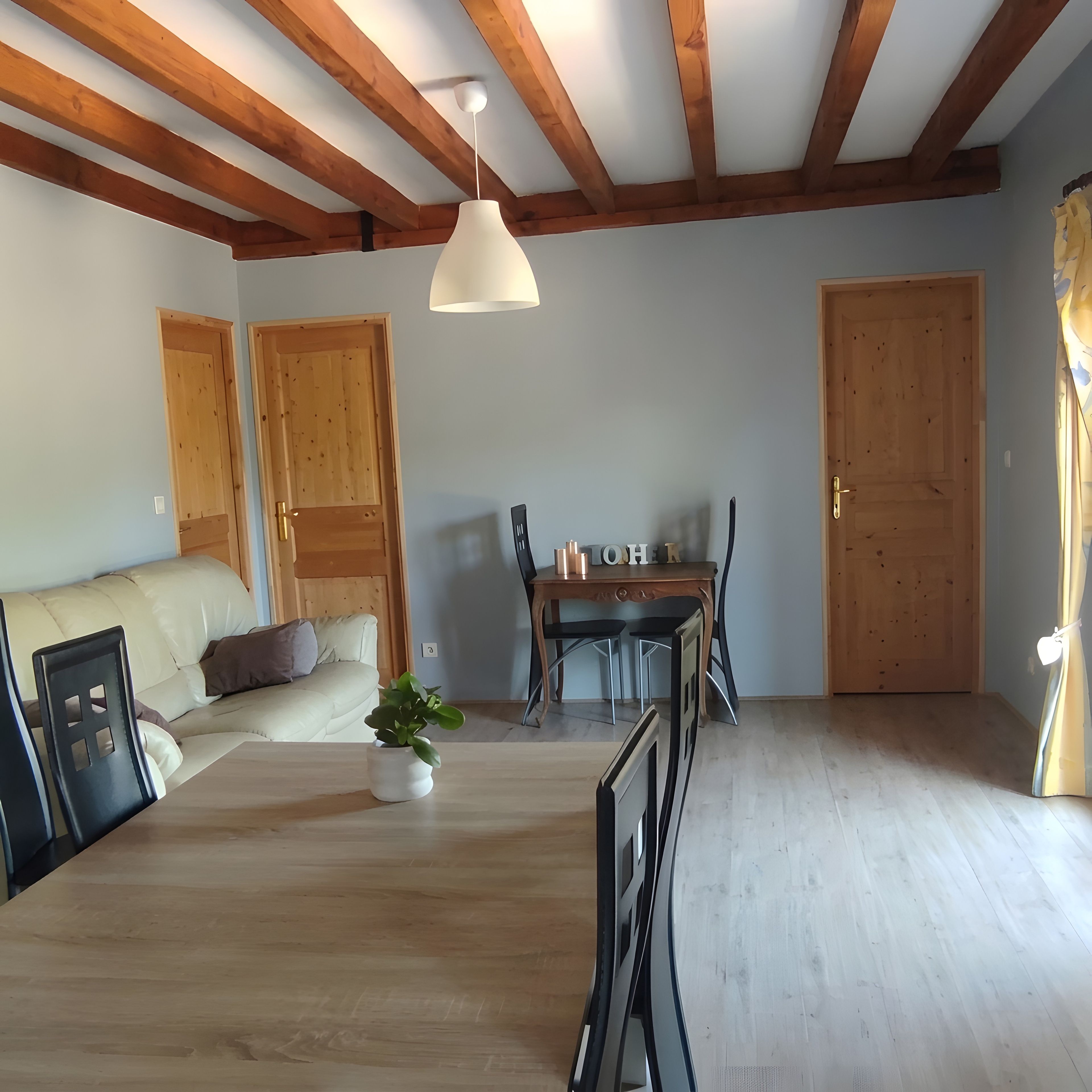Une pièce avec des poutres en bois, un canapé, une table à manger avec des chaises et une porte.