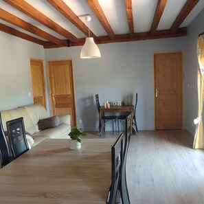 A room with wooden beams, a sofa, a dining table with chairs, and a door.