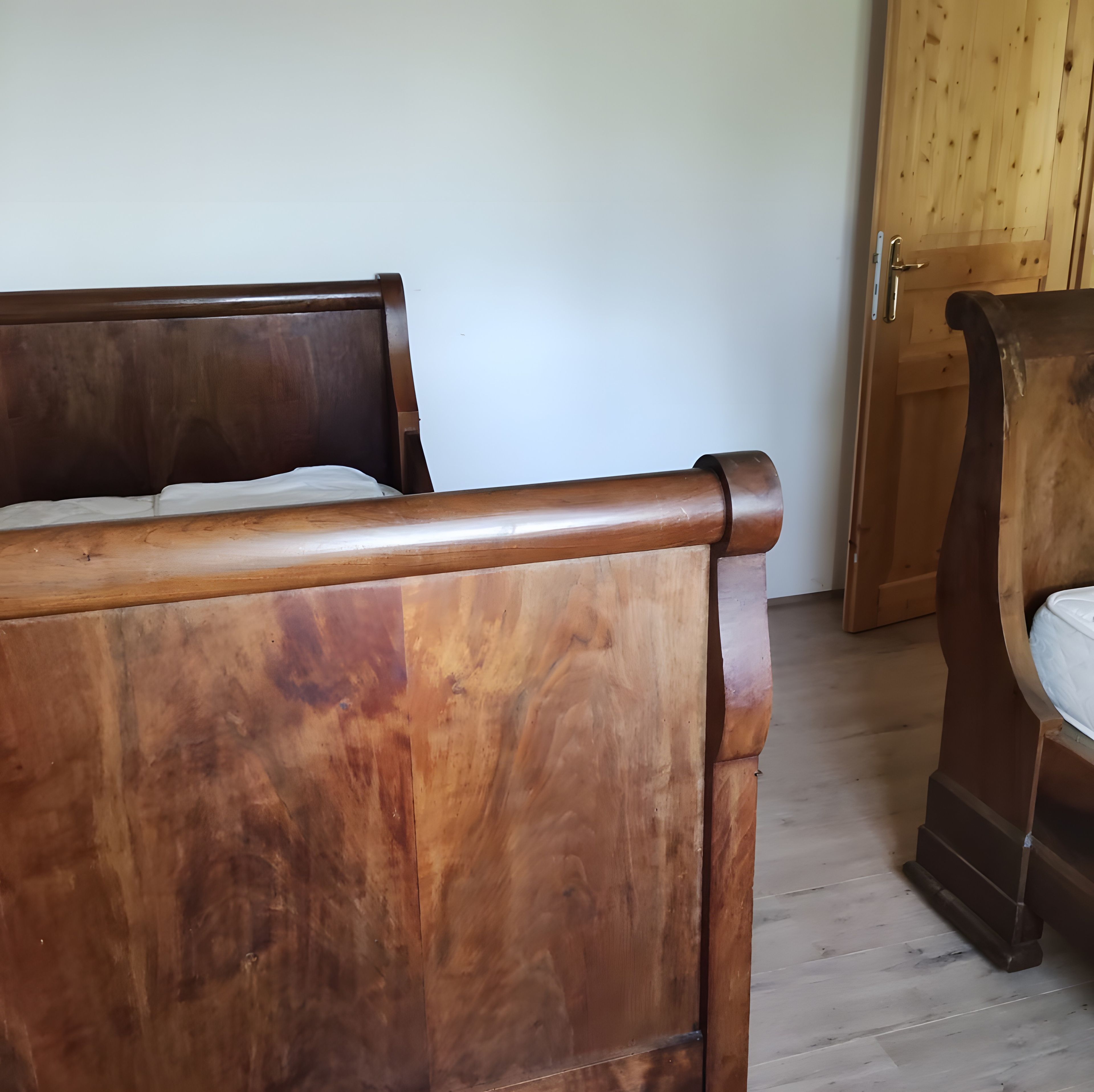 Un lit en bois, doté d’une tête de lit et d’un pied de lit, se trouve dans une pièce avec une porte en bois et un mur blanc.
