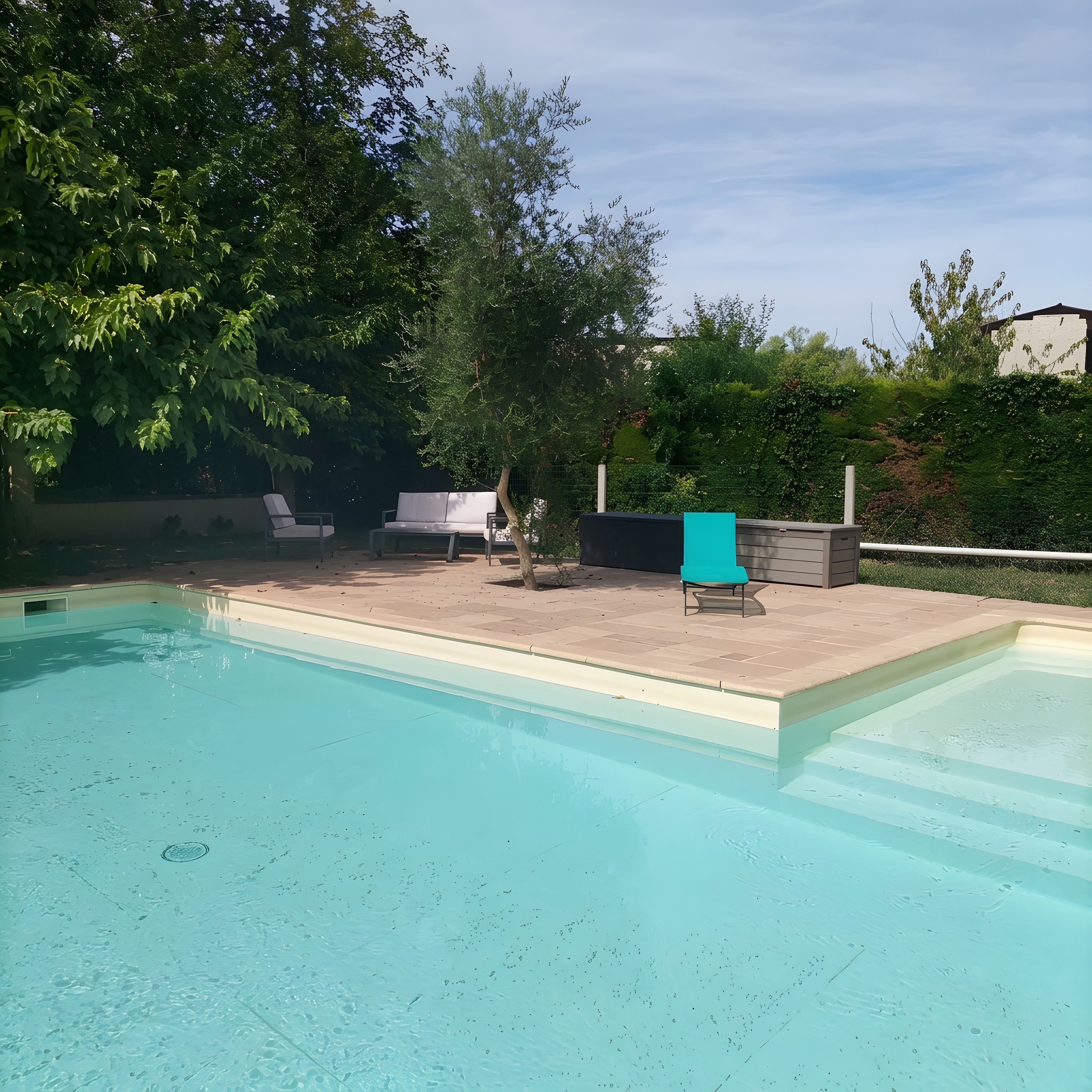 Una piscina con solárium empedrado, rodeada de follaje y algunas tumbonas.