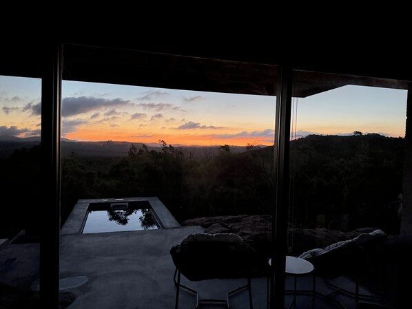 A modern outdoor seating area with a view of a sunset over a mountainous landscape.