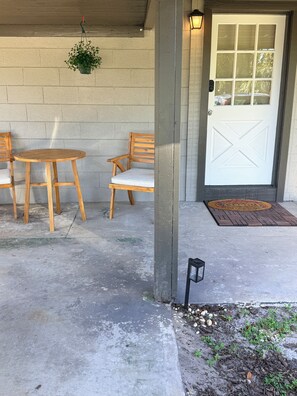 A concrete patio with two wooden chairs and a table, a white door with a window, and a hanging plant. - Peaceful  studio in charming Orlando  - 5 Min Universal, Great Location. (Orlando)