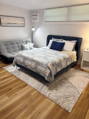 A bedroom with a bed, a sofa, a bedside table, a lamp, and a window with blinds. - Peaceful  studio in charming Orlando  - 5 Min Universal, Great Location. (Orlando)