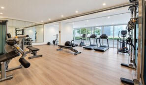 A modern gym with various exercise equipment, large windows, and a wooden floor. - HAVN - High Floor 1 Bed in Business Bay (Dubai)