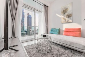 A modern living room with a sofa, a coffee table, and a view of tall buildings. - HAVN - High Floor 1 Bed in Business Bay (Dubai)