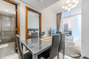 Une chambre d’hôtel moderne dotée d’un coin repas, d’une grande fenêtre offrant une vue sur la ville et d’une douche séparée.