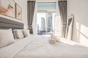 Ein Hotelzimmer mit einem großen Bett, Blick auf hohe Gebäude und einem mit Vorhängen versehenen Fenster.