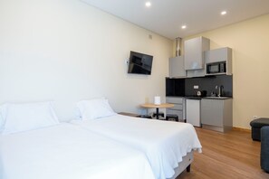 A hotel room with two beds, a small kitchenette, and a flat-screen TV mounted on the wall. - Studio at Campanha Station (Porto)