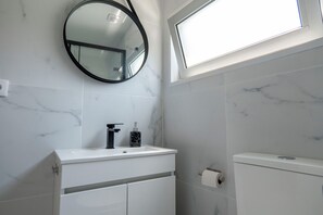 A bathroom with a white vanity, a round mirror, a toilet, and a window above the sink. - Studio at Campanha Station (Porto)