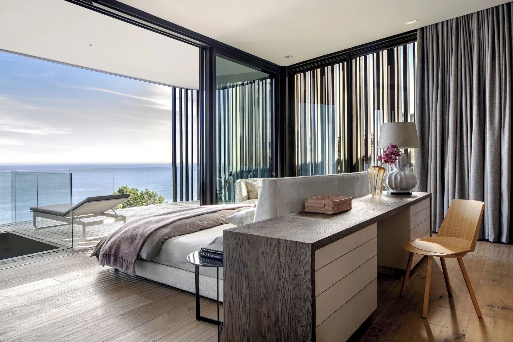 Ein modernes Schlafzimmer mit einem großen Bett, einem Schreibtisch und einem Stuhl, mit Balkonblick auf das Meer.
