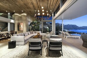 Een moderne woonkamer met een grote bank, twee fauteuils, een salontafel en uitzicht op zee.