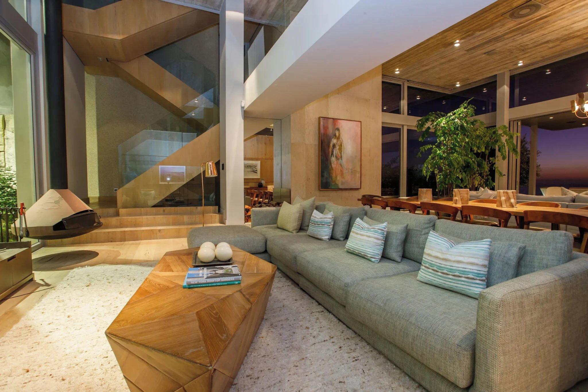 Ein modernes Interieur mit einem Holztisch, einem grauen Sofa mit gestreiften Kissen und einer Treppe, die in ein Obergeschoss führt.