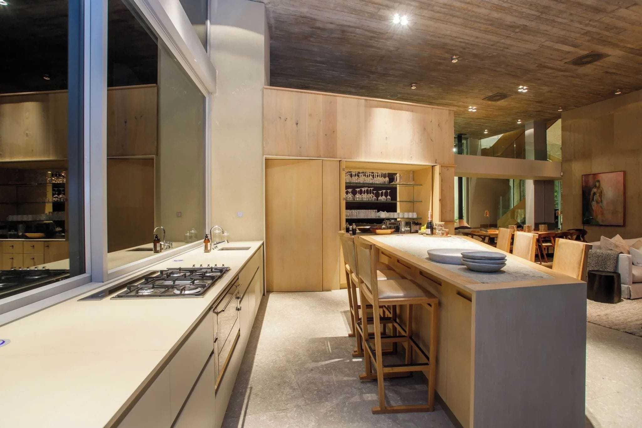 A modern kitchen with a central island, wooden cabinets, and a large window.